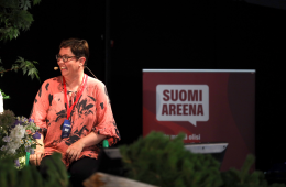 Merja Kyllönen on puhujana Suomi Areenassa ja katsoo vasemmalle hymyillen.